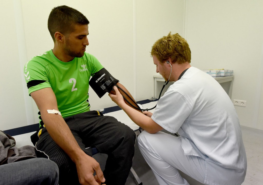 Doctor Alexander Humberg (R) from Luebeck looks at a refugee from Iraq in the primary health care centre that is currently placed in containers in Rendsburg, Germany, 20 August 2015. More than 60 doctors and nurses from the university hospitals in Kiel and Luebeck started their voluntary service to take care of the refugees in the new reception centre. Photo:†CARSTEN†REHDER/dpa