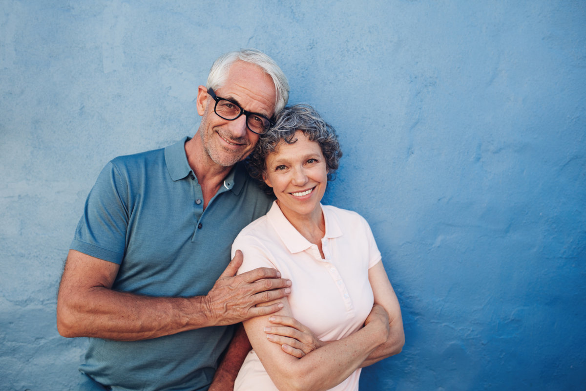 Portrait of smiling mature couple standing together against blue background. Happy middle aged man and woman against a wall.